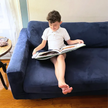Child enjoying The Read To Me: Recordable Book Buddy on a blue sofa, combining reading with interactive audiobooks for kids.