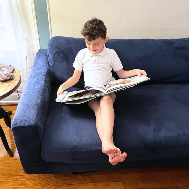 Child enjoying The Read To Me: Recordable Book Buddy on a blue sofa, combining reading with interactive audiobooks for kids.