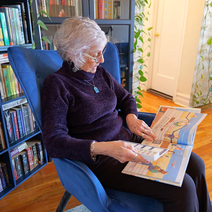 Elderly woman enjoying The Read To Me: Recordable Book Buddy in cozy chair, surrounded by bookshelves, enhancing audiobook...
